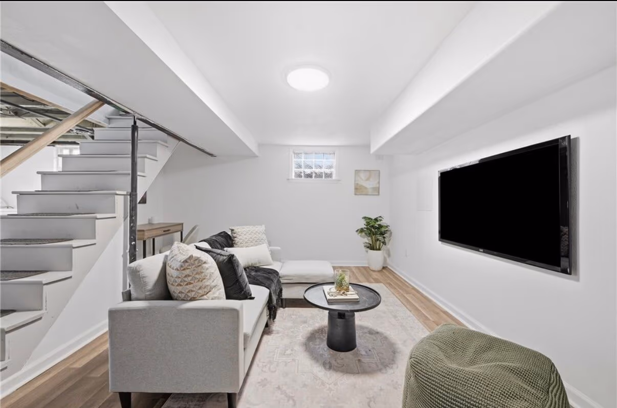 Finished basement living area with a staircase, seating, and wall-mounted TV
