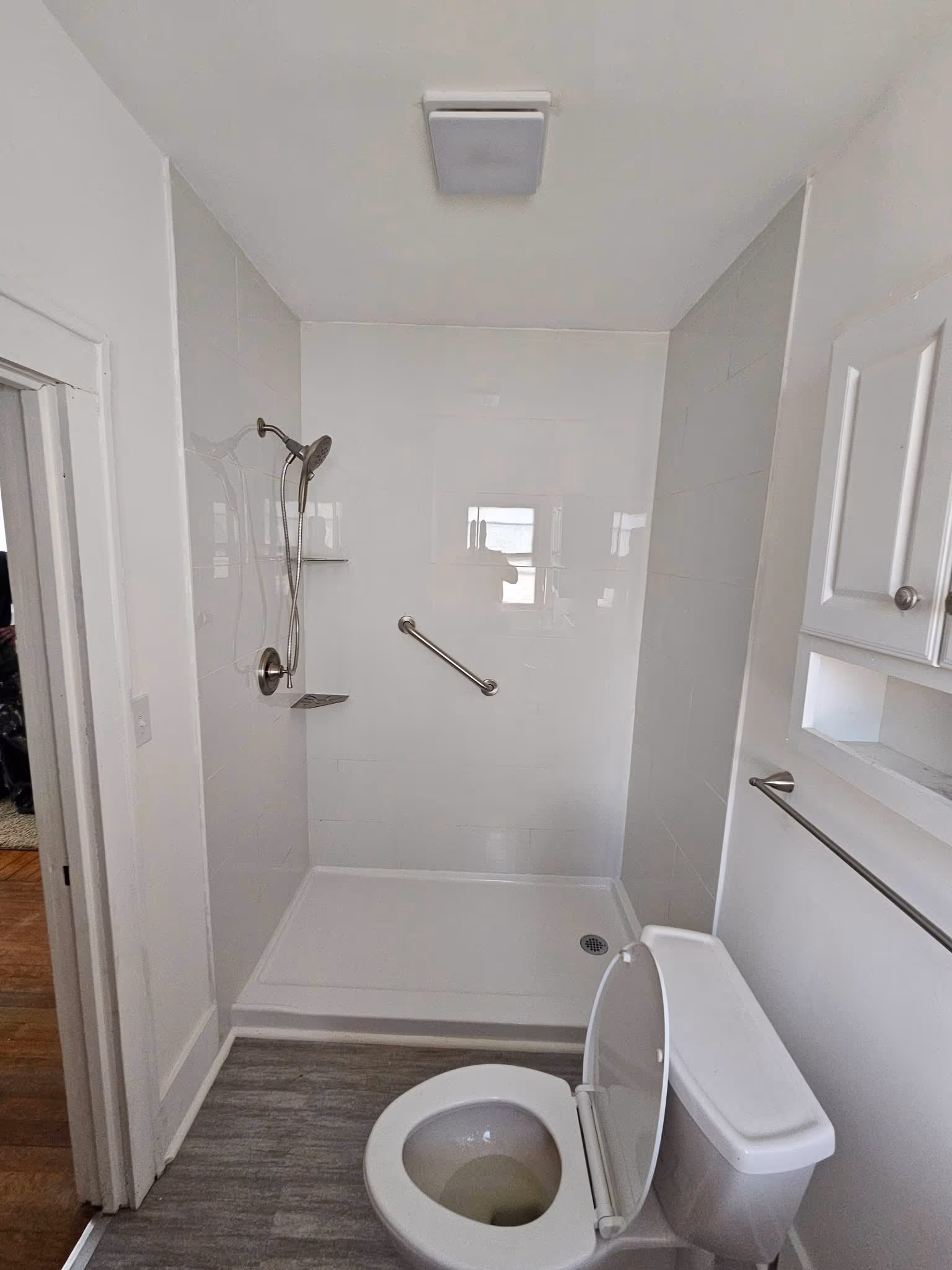 Finished bathroom with a low-threshold tub and shower, grab bars, storage cabinet, and wood-look flooring