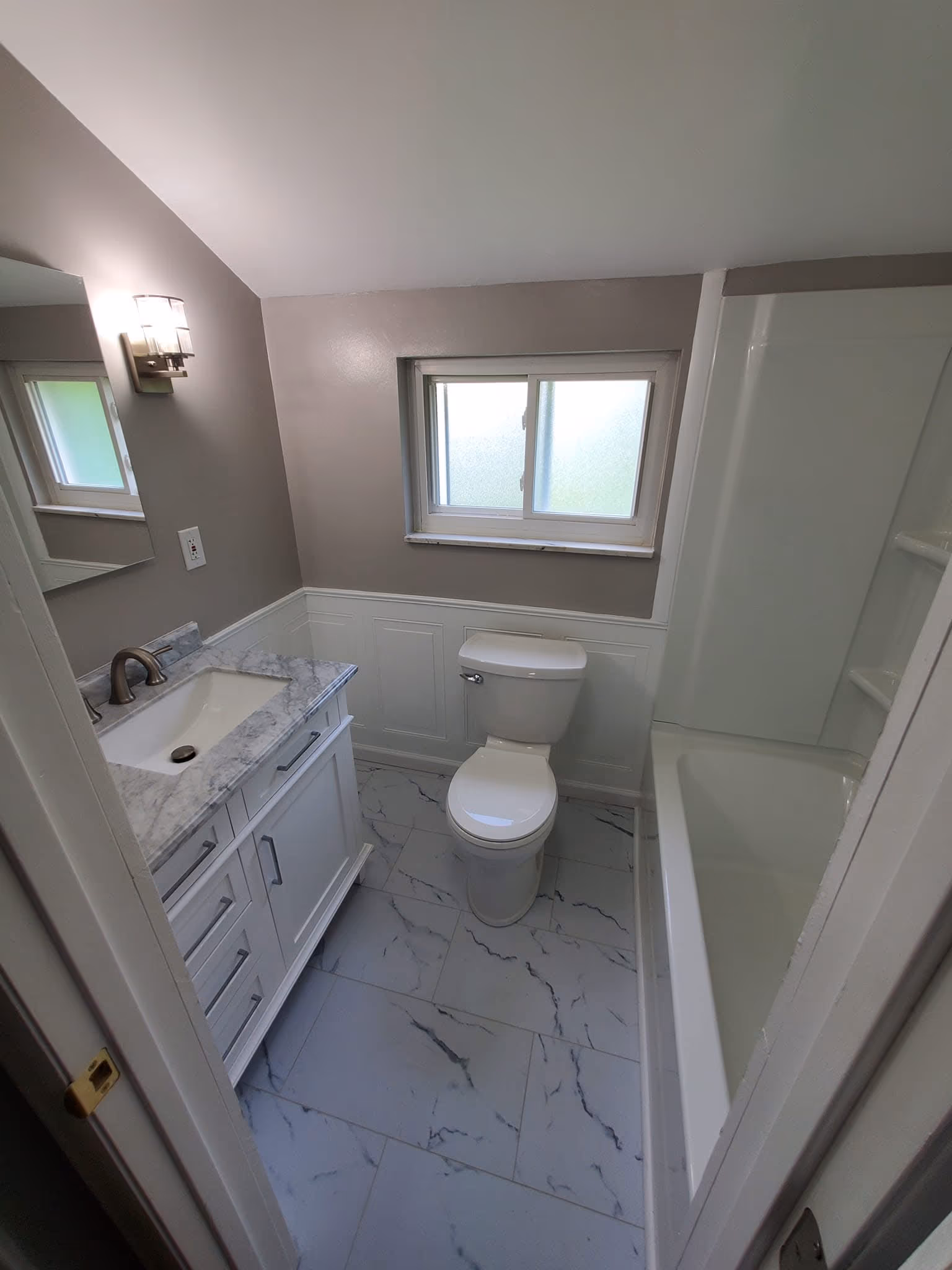 Finished gray bathroom with a white vanity, bathtub, and marble-look floor tile
