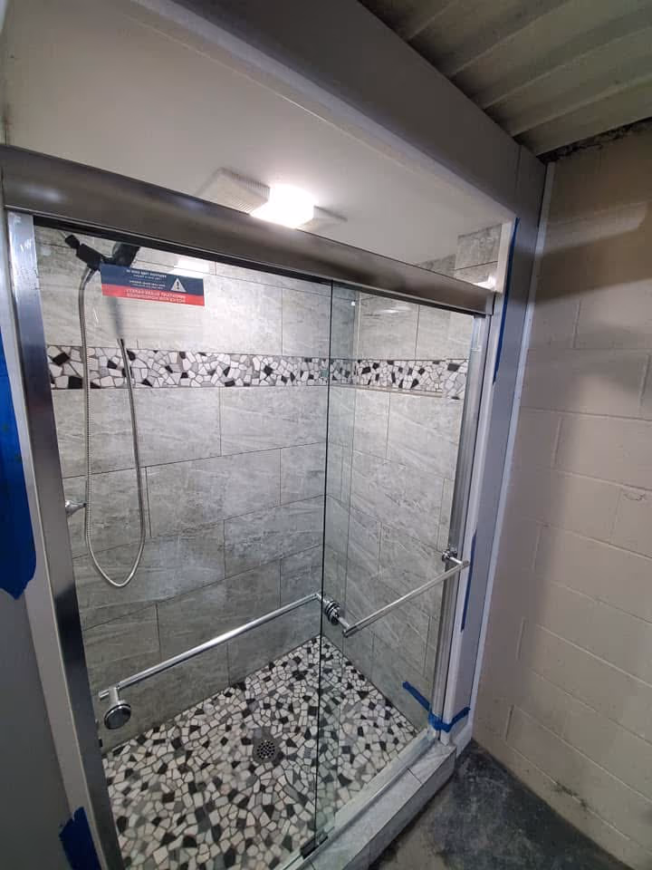 Finished glass walk-in shower with gray wall tile, mosaic floor tile, niche, and sliding door