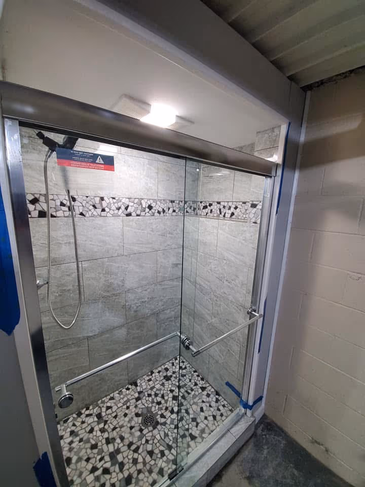 Finished glass walk-in shower with gray wall tile, mosaic floor tile, niche, and sliding door
