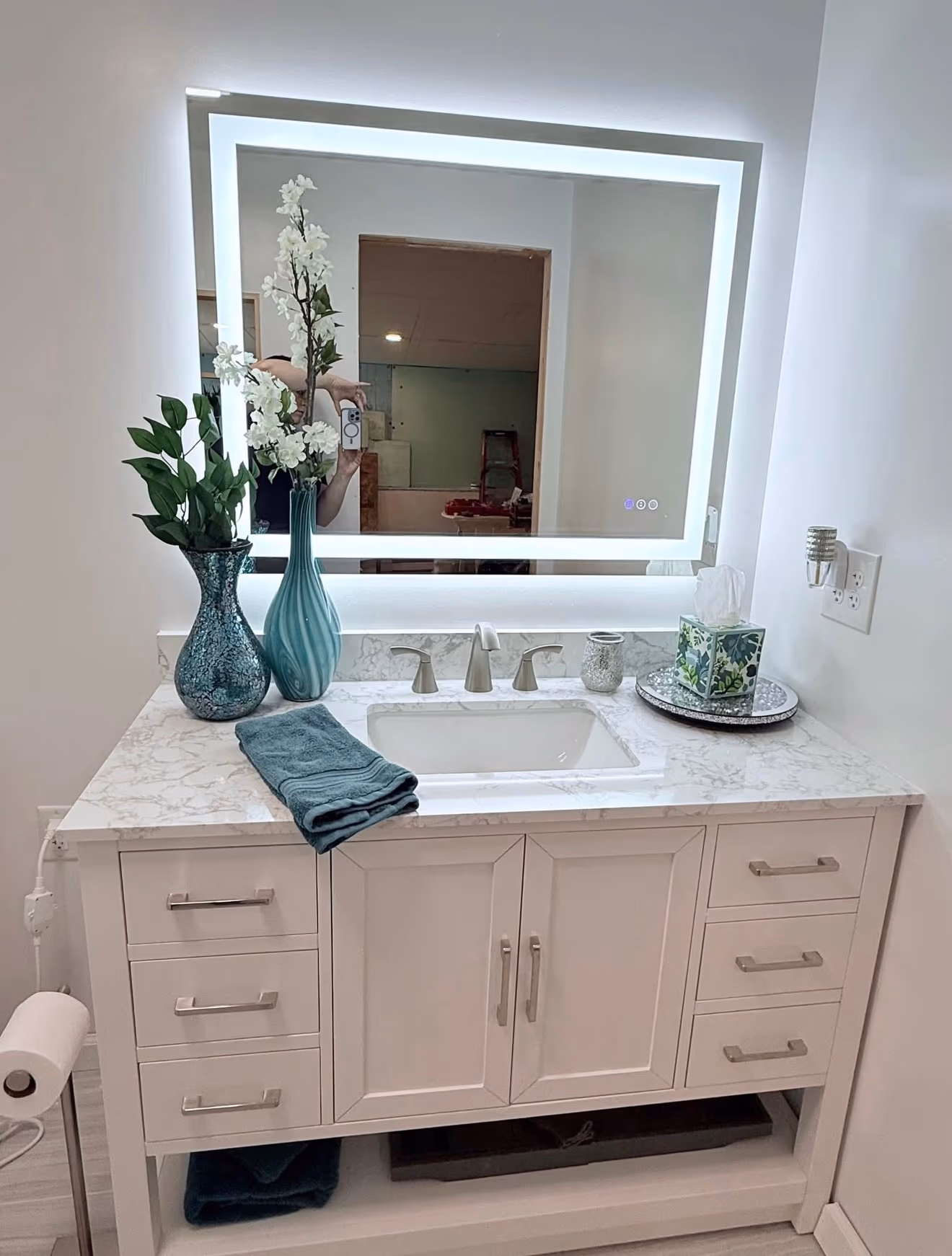 Finished bathroom with a white double vanity, marble-look countertop, and illuminated mirror