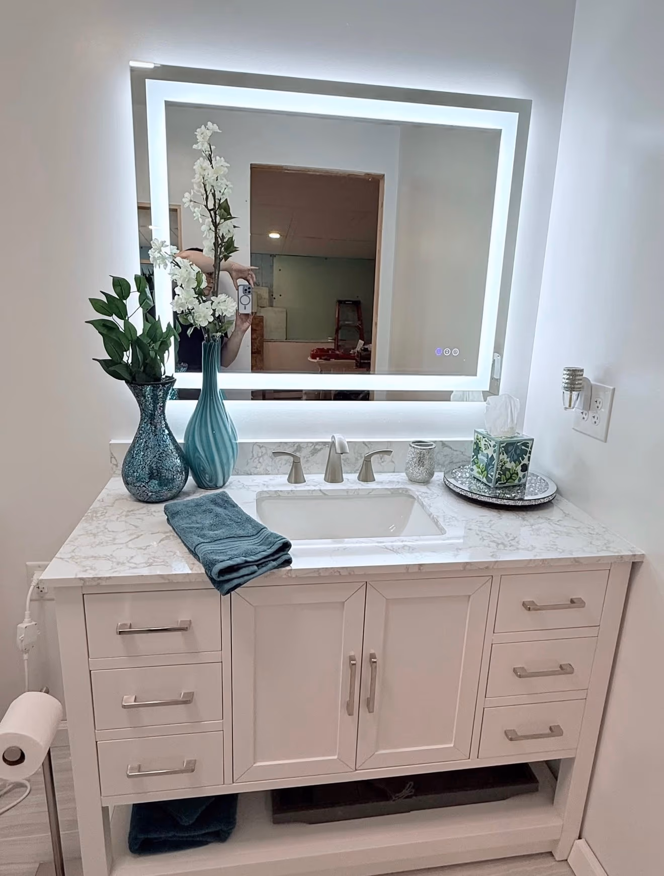 Finished bathroom with a white double vanity, marble-look countertop, and illuminated mirror